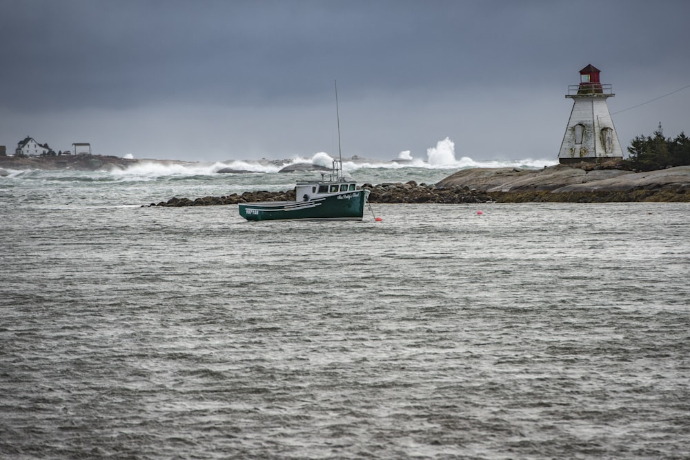 teal boat on body of water near lighthouse