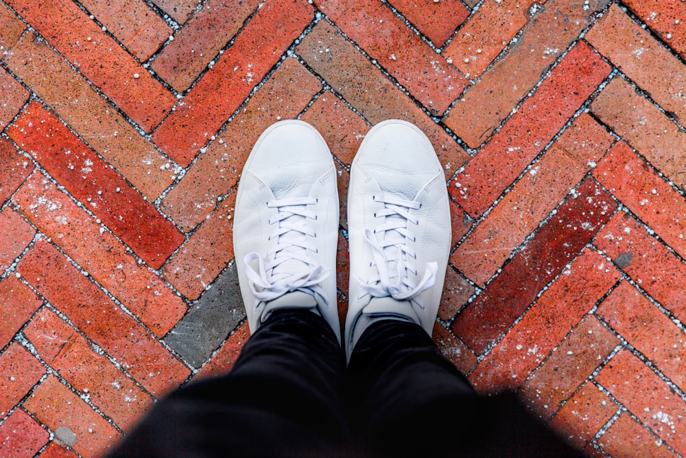 personne portant des baskets blanches debout sur un sol de briques brunes