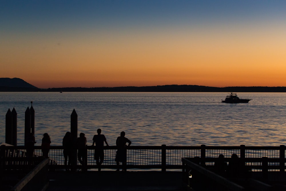 silhouette of people standing on dock during sunset