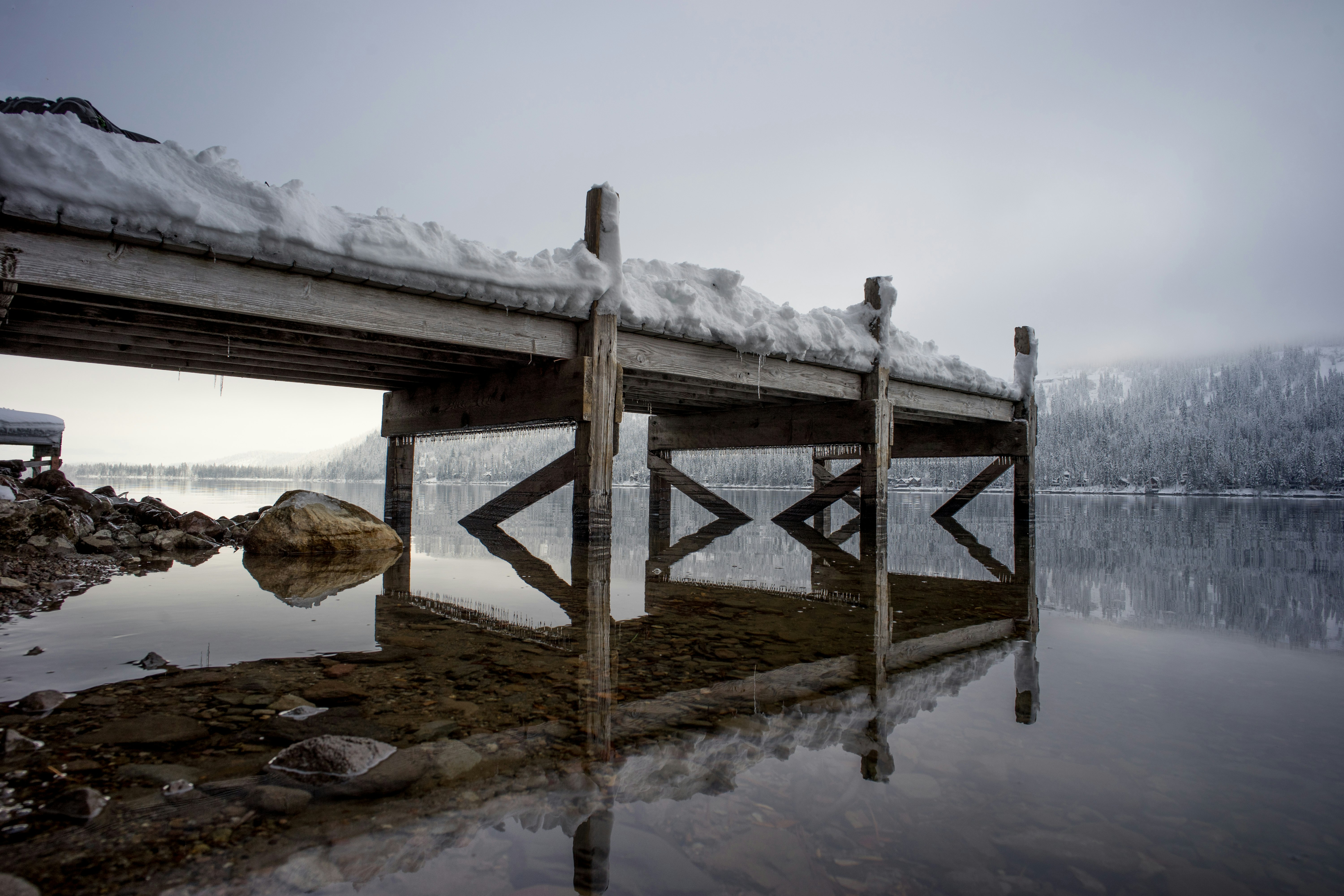 snow on brown wooden dock near body of water