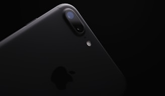 A close-up angle of a sleek black smartphone showcasing dual-lens camera and a flash along with the iconic logo in a minimalist and elegant design. The background is dark, emphasizing the device's polished finish.