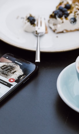 teal ceramic teacup on saucer beside black smartphone