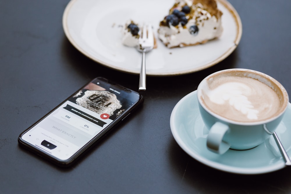 teal ceramic teacup on saucer beside black smartphone