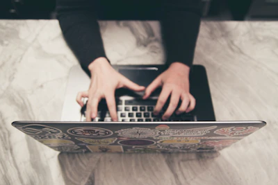 Close-up of hands typing on a laptop keyboard with moon phase stickers around.