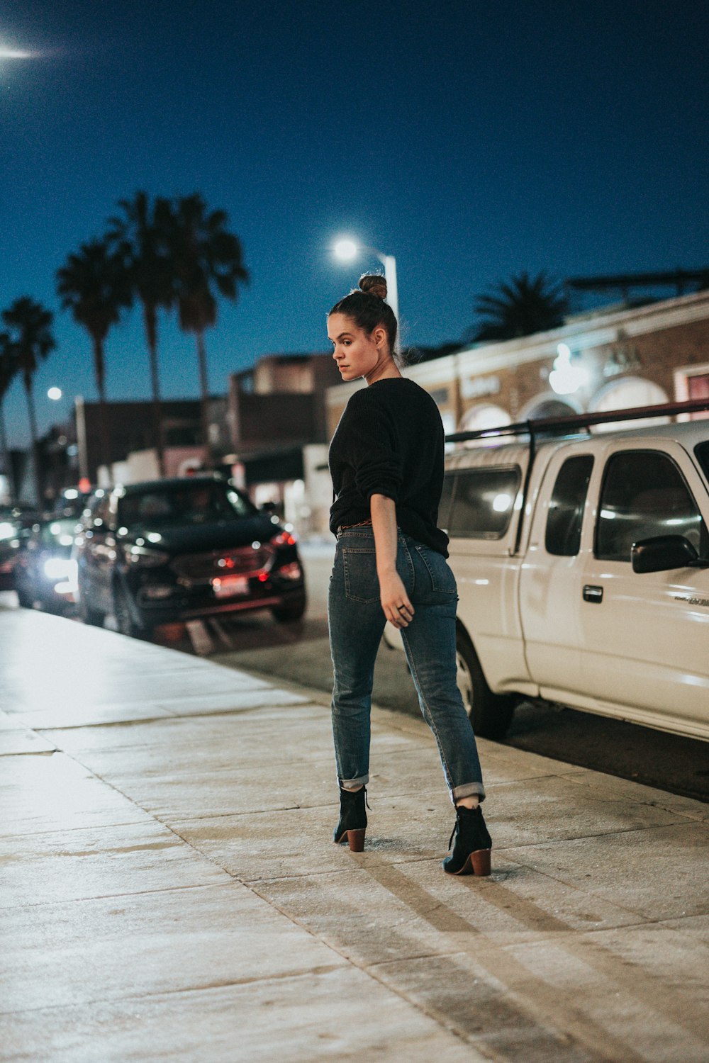 women's wearing in black top and blue denim jeans walks on brown concrete pathway beside road with vehicles