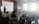 A group of people are seated in a room with exposed brick walls and large windows. Rays of sunlight illuminate the space. A presenter stands in front of a projection screen displaying a slide in Russian, and a flipchart is nearby.