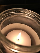 Close-up of a sleek glass candle container with a soft glowing flame inside.