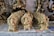 Several small intricately designed brass statues are placed on a surface covered with newspaper. The statues are mostly of Hindu deities, showcasing details such as ornate crowns and intricate carvings. The statues are arranged in rows, with larger statues in the background.