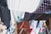 Colorful fabrics with various patterns, such as polka dots and floral designs, are hanging on wooden racks and lines. They create a vibrant tapestry of colors and textures, with the sunlight casting dynamic shadows between them.