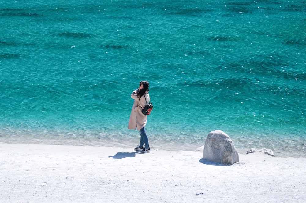 woman in brown coat beside body of water during daytime