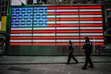 two man walks near USA flag wall