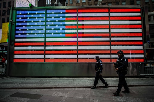 two man walks near USA flag wall