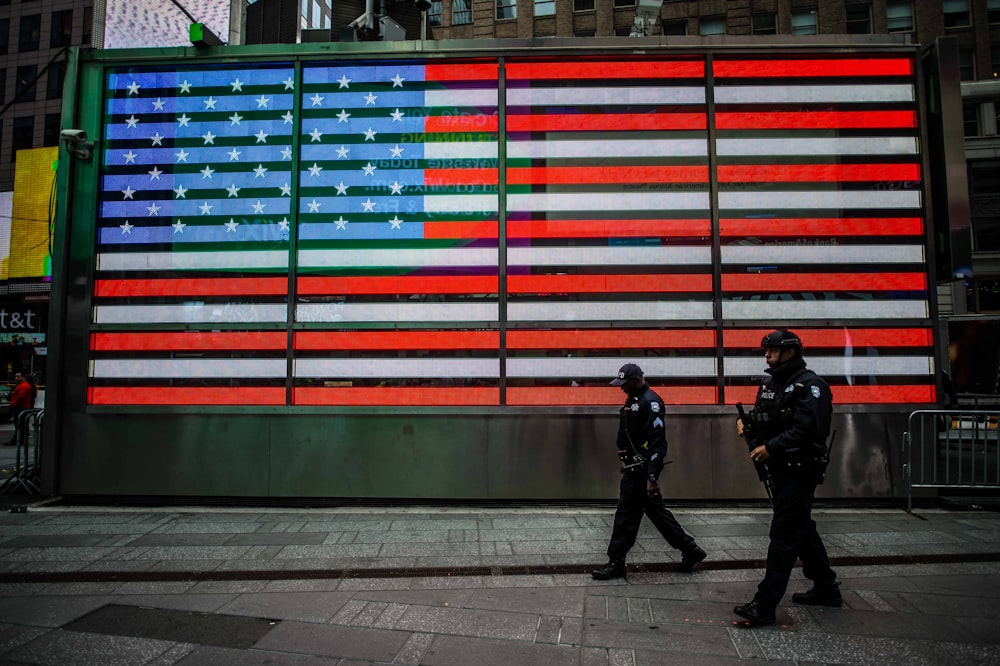 두 남자가 미국 국기 벽 근처를 걷는다.