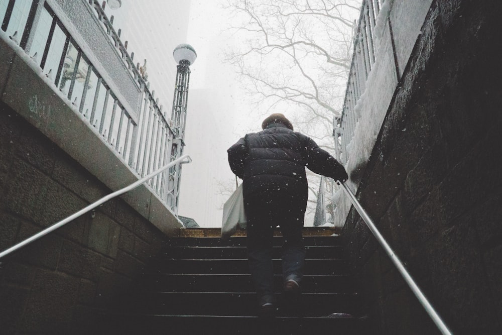 person walking on stairway holding on railings under cloudy sky