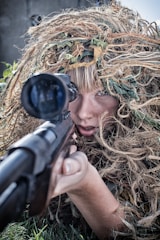 woman wearing gillie suit holding sniper rifle