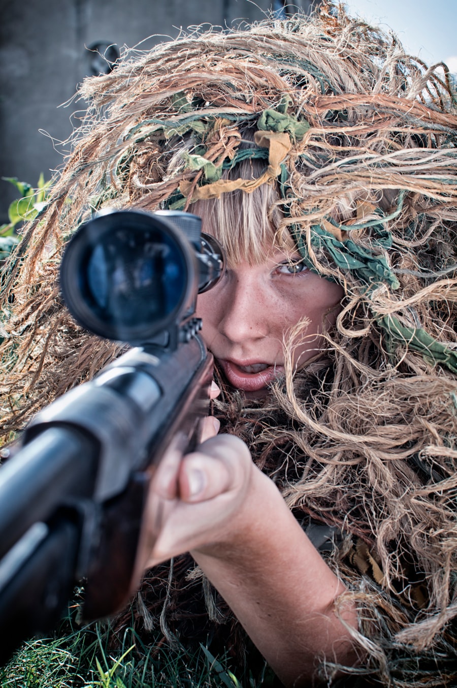 A woman in camouflage points a sniper rifle at a location off-camera.
