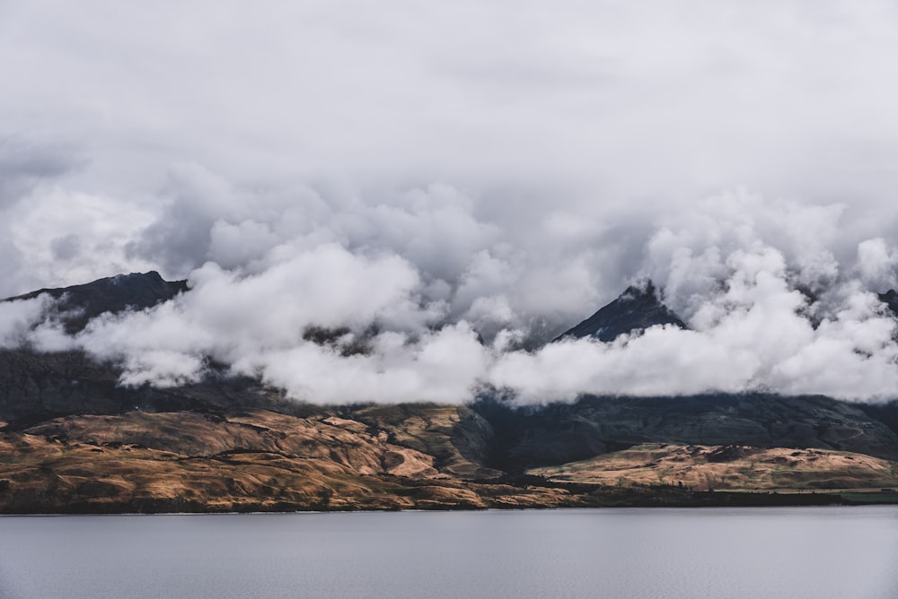 mountain covered with clouds near body of water