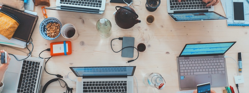 Cluttered desk with computers, phones, beverages, and personal items, as at a workshop or hackathon