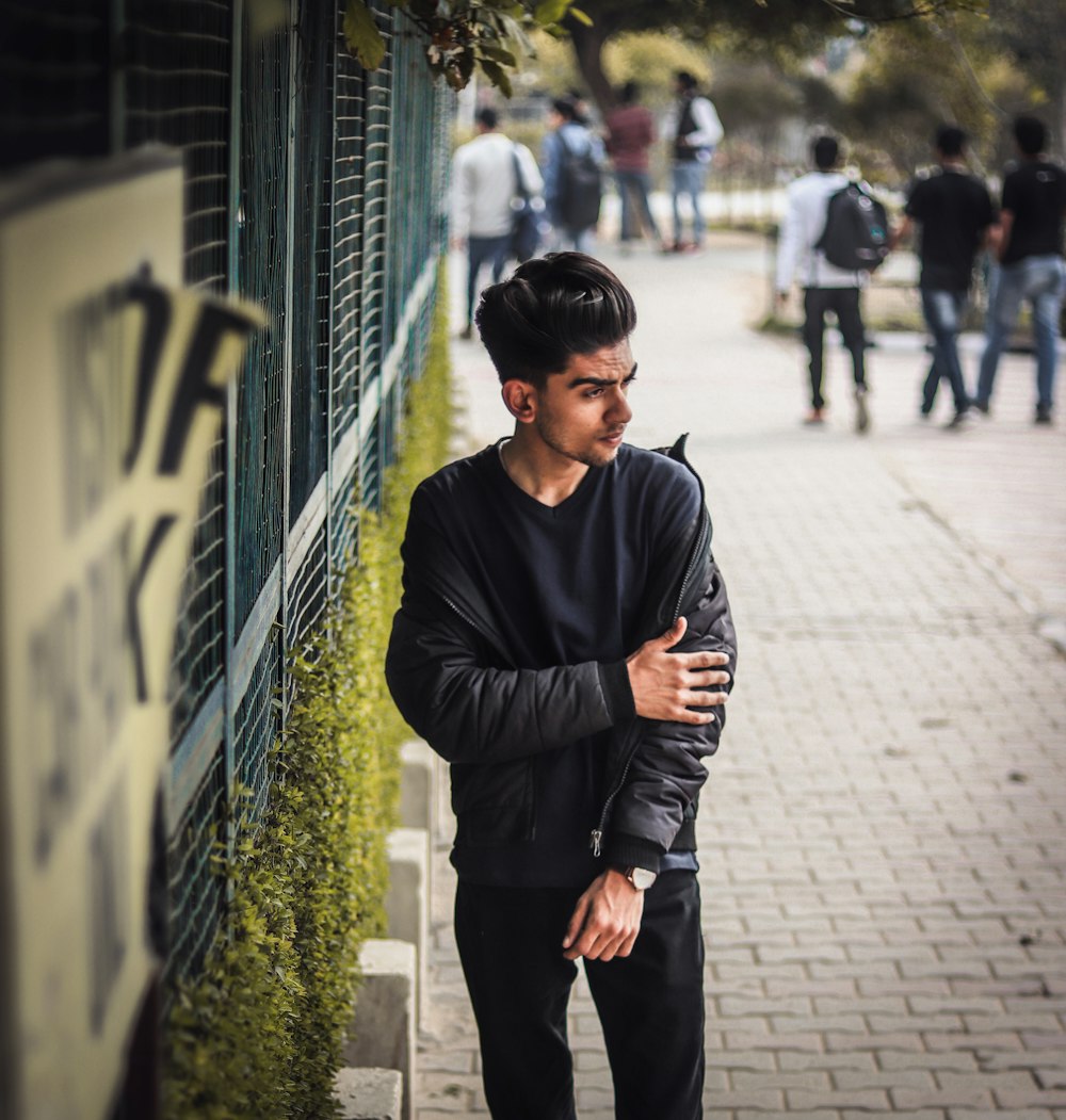 man in black sweater standing beside blue metal fence during daytime