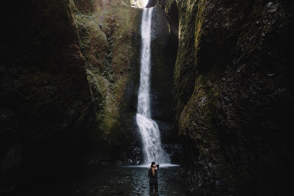 person stands in front of waterfalls during daytime