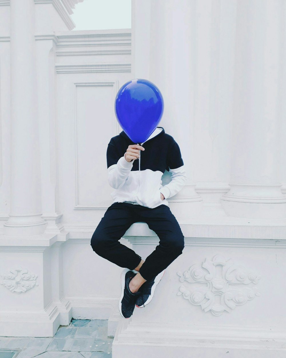 Person, die tagsüber auf weißem Betonpflaster sitzt und einen blauen Ballon hält