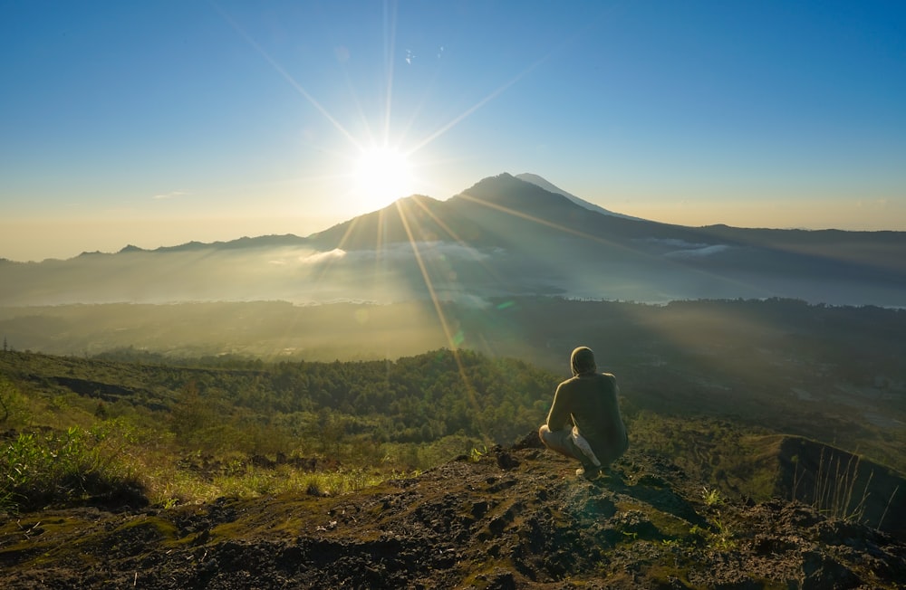 man squatting on mountain top during daytime