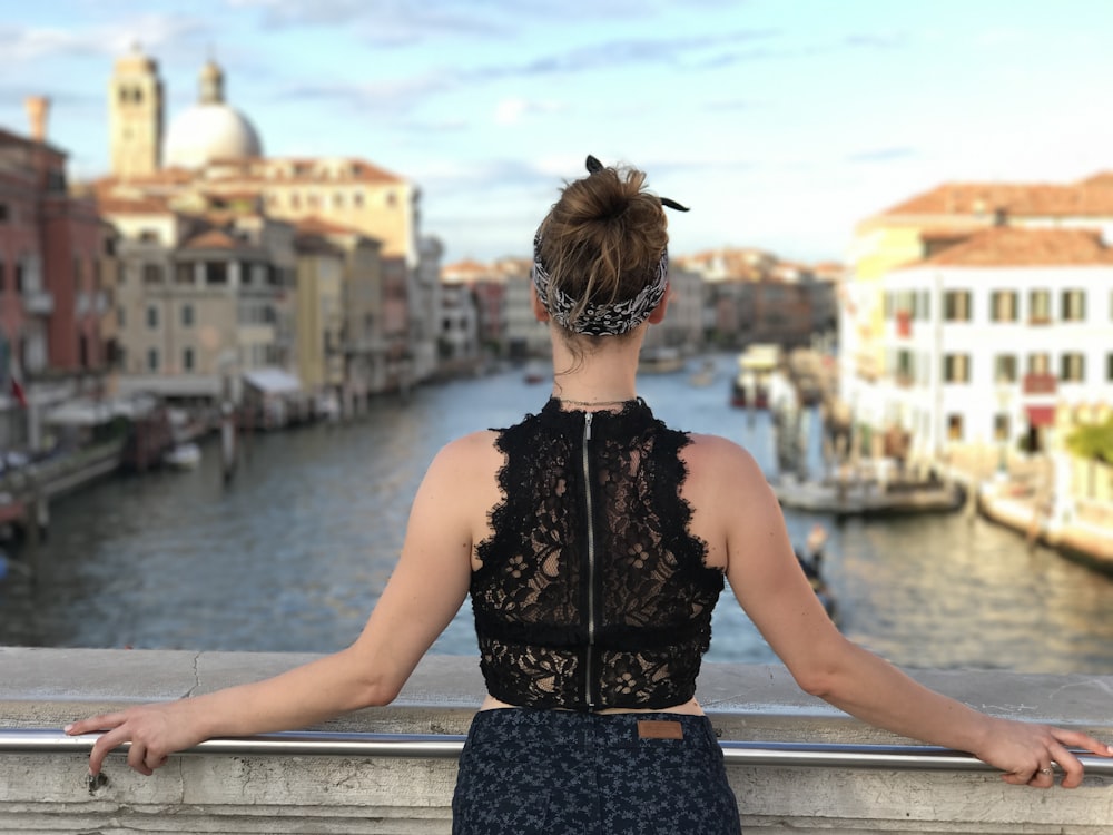 Fotografia a fuoco selettiva di donna che tiene il corrimano in metallo grigio sullo specchio d'acqua durante il giorno