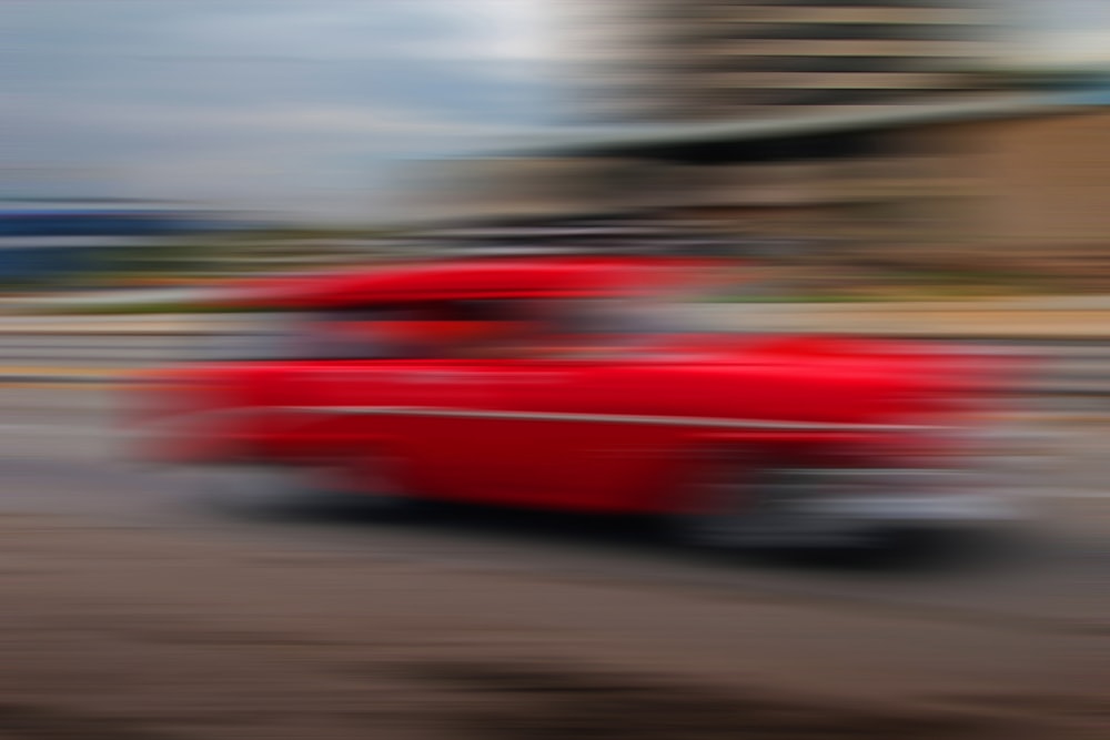 a red car driving down a street next to a tall building