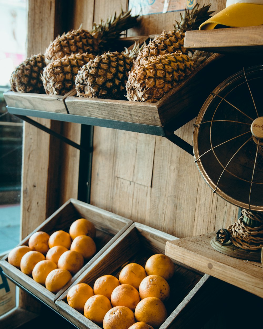 pineapple and orange fruits on brown wooden rack