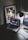 A modern workspace features a laptop displaying a music streaming platform, accompanied by a desk lamp, a keyboard, and a smartphone. A framed abstract art piece with geometric shapes and bold colors is propped against the wall.