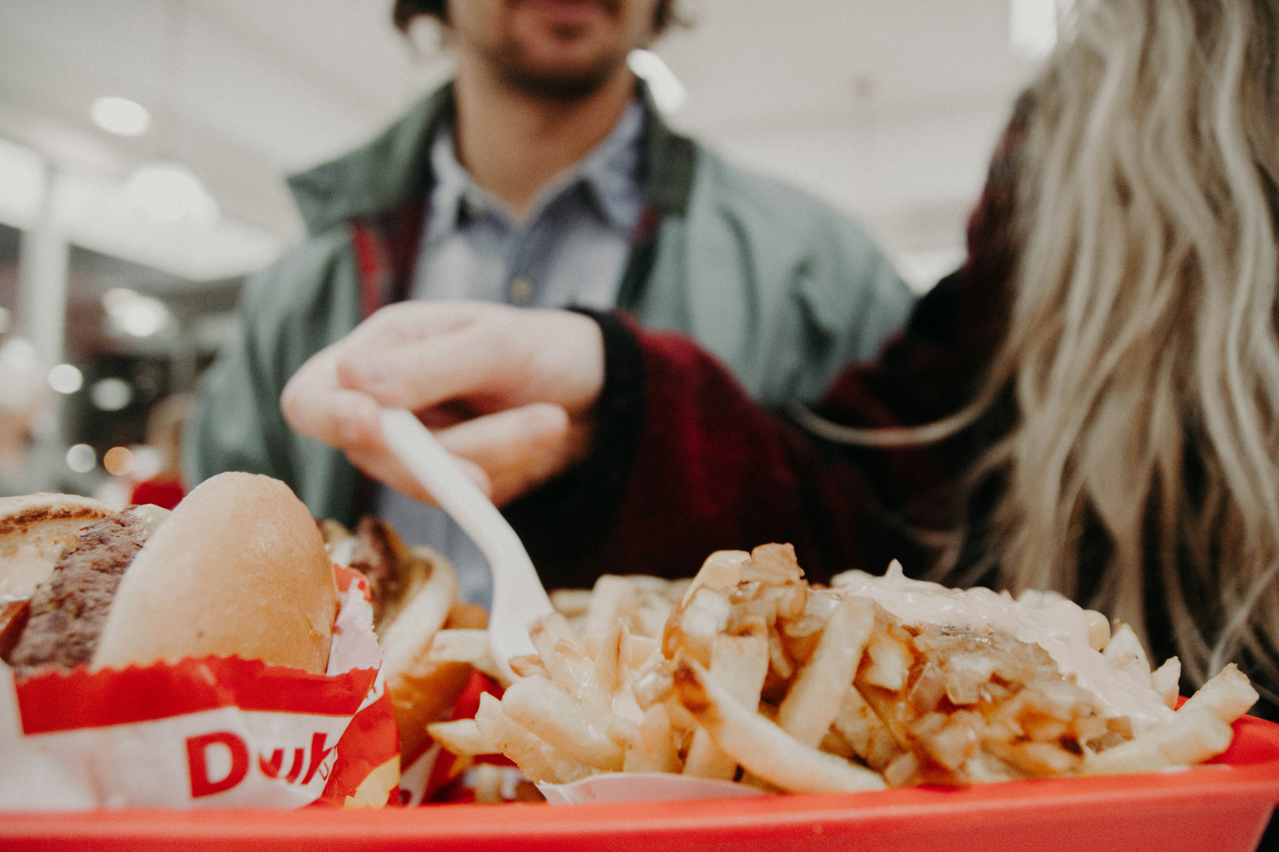 woman in maroon long-sleeved shirt holding fork over fries