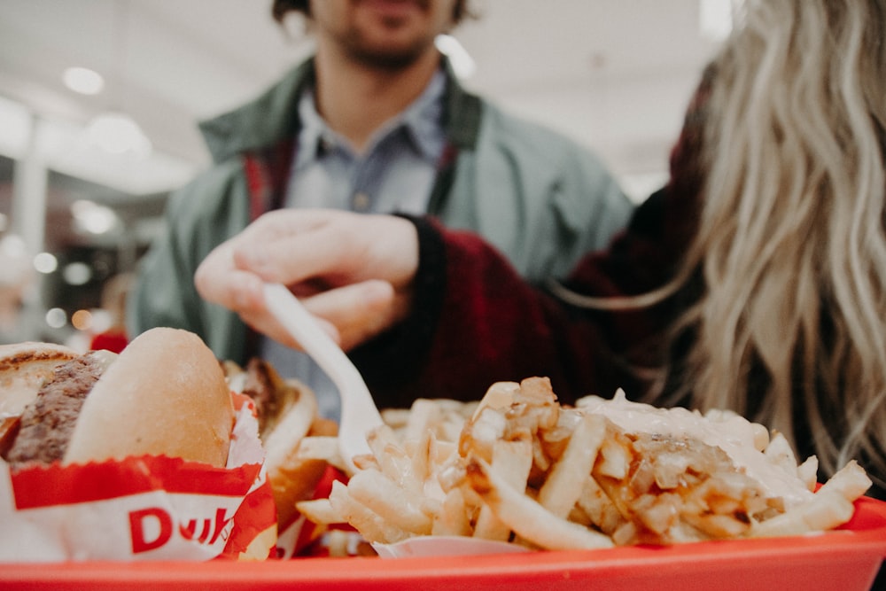 woman in maroon long-sleeved shirt holding fork over fries