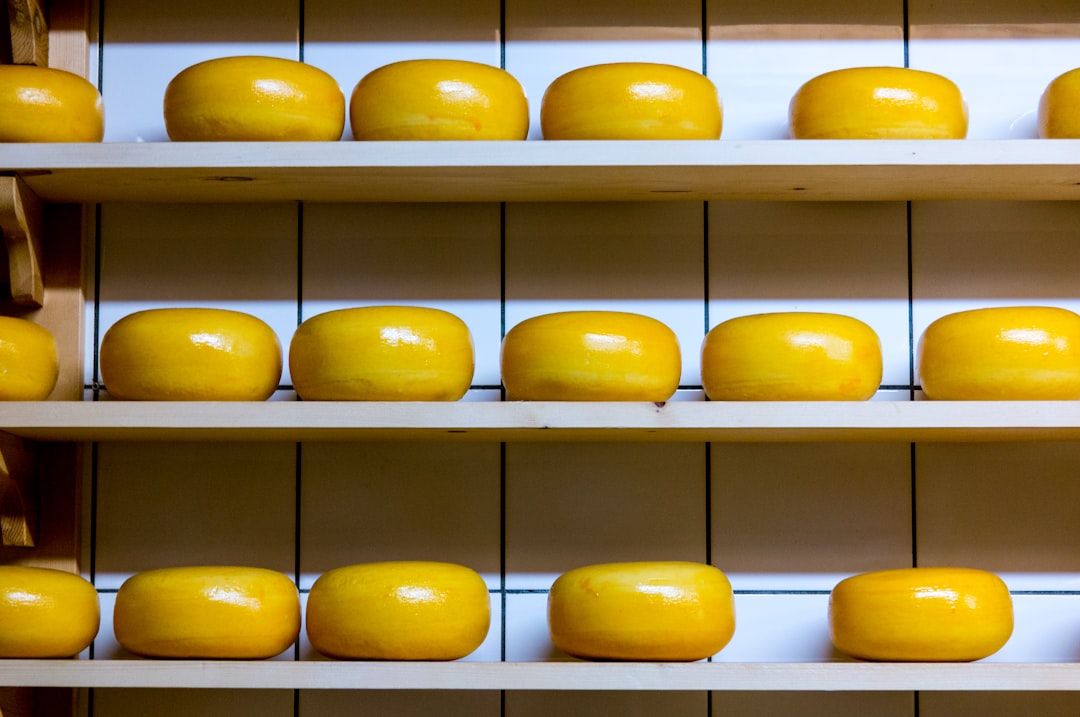 yellow cheese lot on brown wooden shelf, Cheese wheels like (slightly yellow) teeth in a row. It makes my smile.