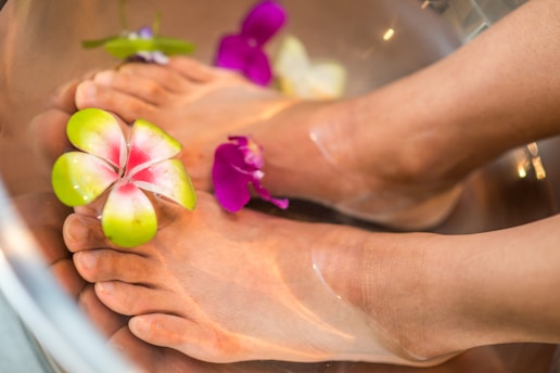 Feet soaking in a modern spa basin surrounded by soft candlelight and plush towels.
