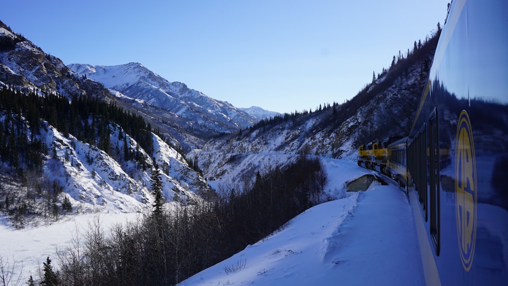 blue and yellow locomotive travelling through mountains covered with snow