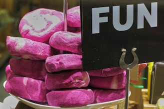 A stack of vibrant pink bagels or doughnuts are piled on a white dish with a sign labeled 'FUN' beside them.