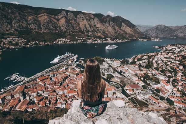 woman sitting on top of cliff facing buildings