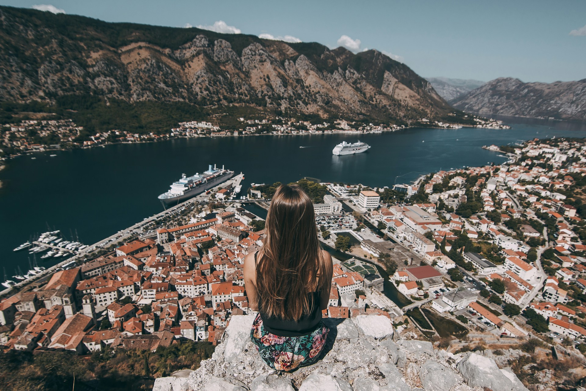 woman sitting on top of cliff facing buildings