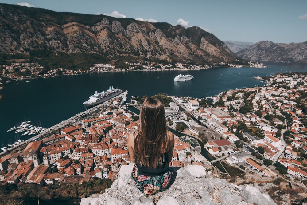 woman sitting on top of cliff facing buildings