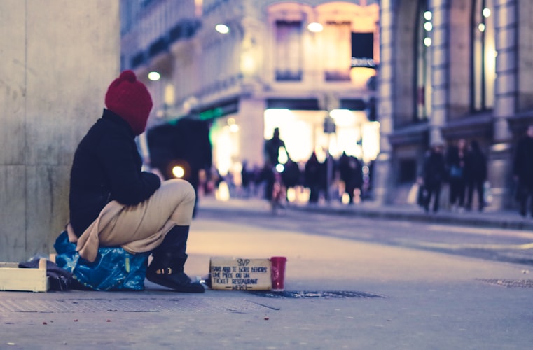 The real issue for the NIMBY's of the world is lack of supports A photo of a person sitting on the side of a building in a downtown, commercial area - it appears they are homeless.