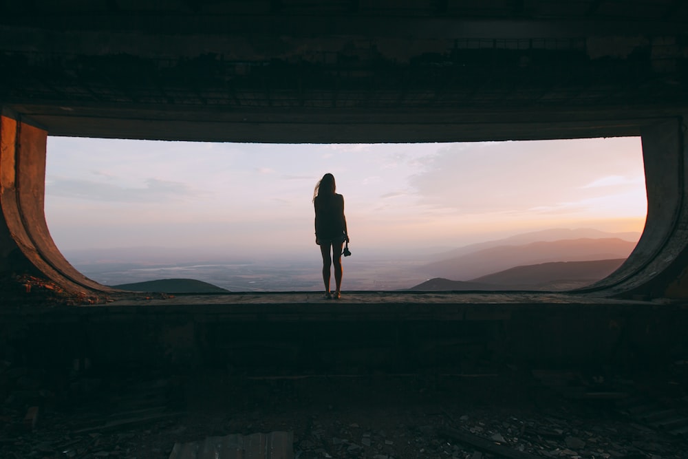 Silhouette einer Frau, die am Rand steht und auf Berge blickt