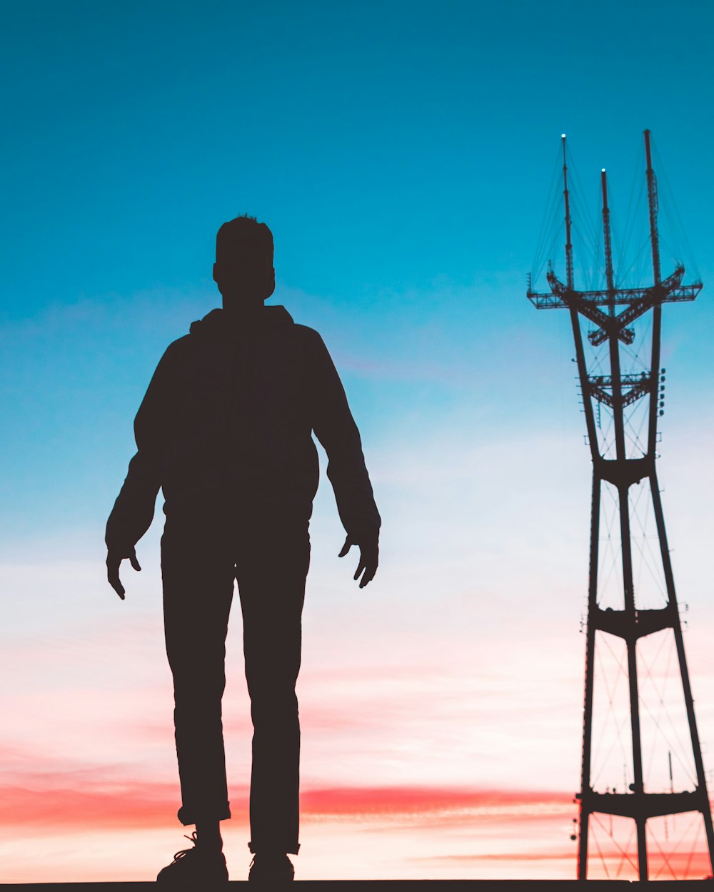 silhouette photography of man standing in front of transmission tower