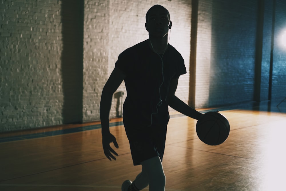 Homem driblando bola em quadra de basquete fechada