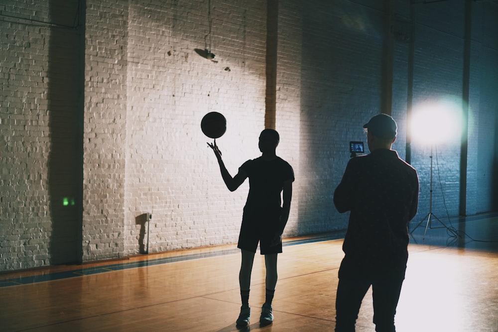 man capturing silhouette photo of man spinning basketball