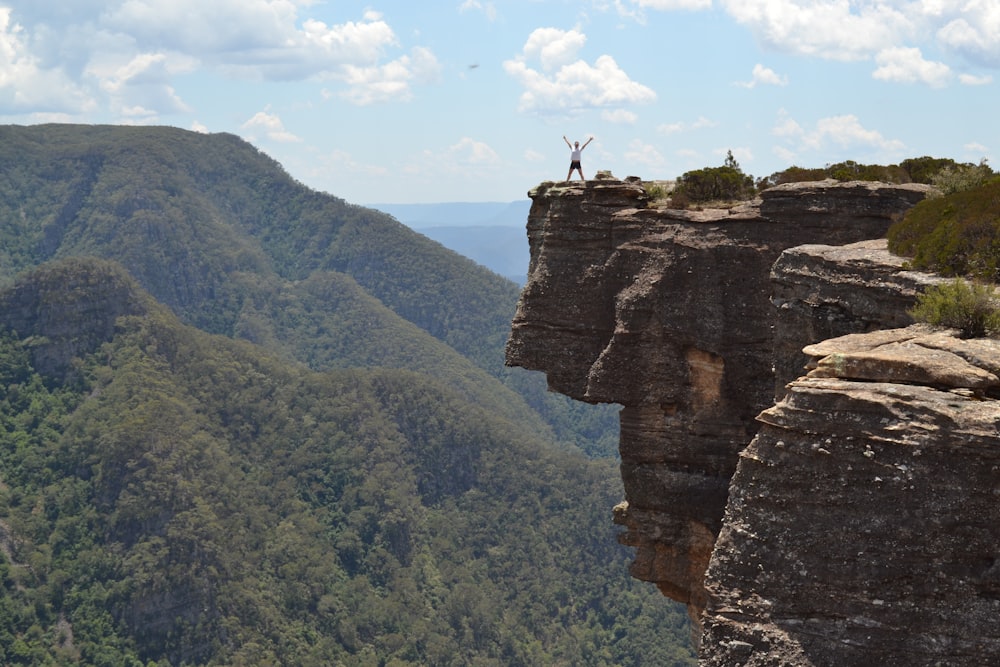 person standing on edge of stone cliff with green mountain in the background