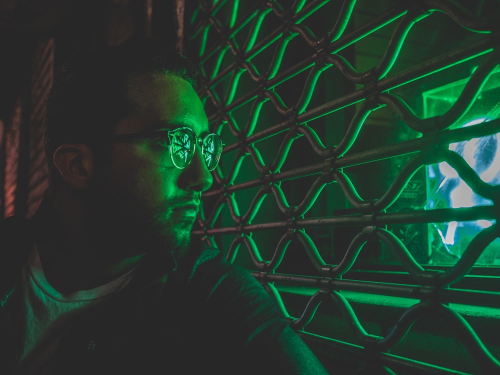 man wearing eyeglasses sitting near window grill inside dim-lighted room