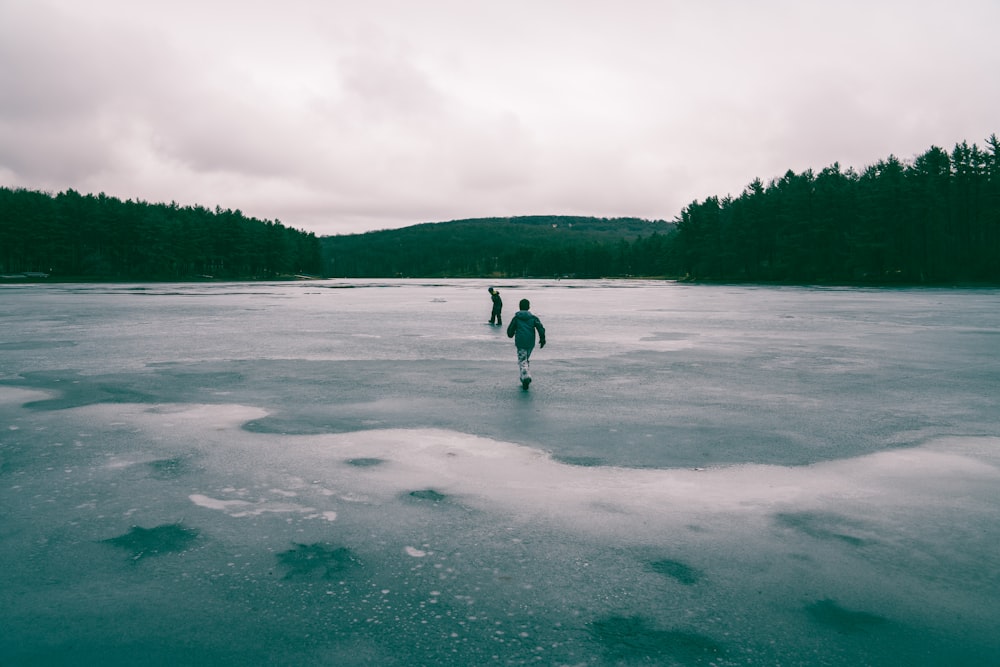 two people in middle of frozen body of water near trees