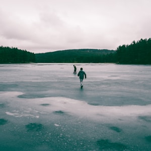 two people in middle of frozen body of water near trees
