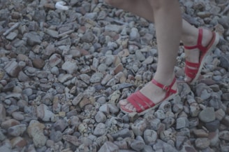 A person wearing red sandals walks on a surface covered with variously sized smooth stones or pebbles.