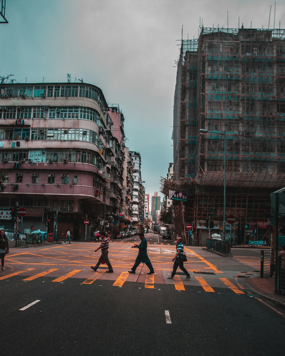 three men crossing road in front of two buildings during daytime